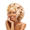 A woman wearing a satin sleeping cap tied in a bow, smiling and touching her face.