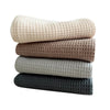 A stack of four absorbent 100% cotton waffle weave towels in beige, brown, gray, and black.