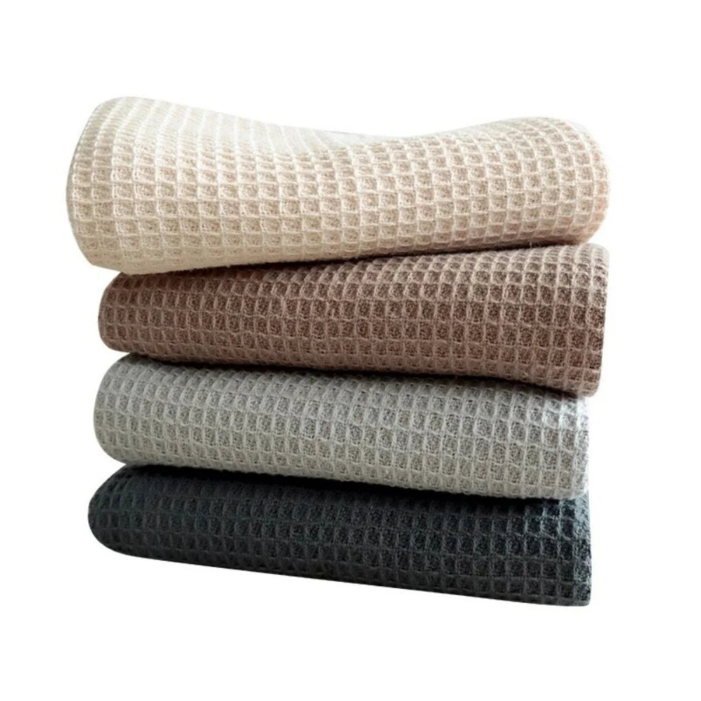 A stack of four absorbent 100% cotton waffle weave towels in beige, brown, gray, and black.
