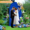 A couple is embracing in front of a blue wedding arch covered with colorful flowers and greenery.