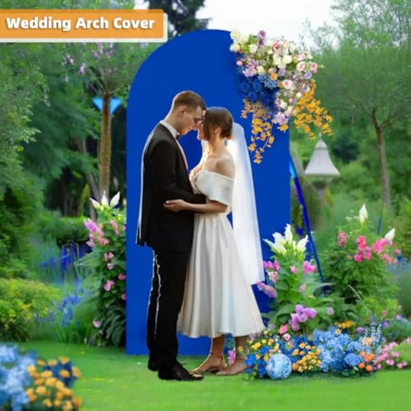 A couple is embracing in front of a blue wedding arch covered with colorful flowers and greenery.
