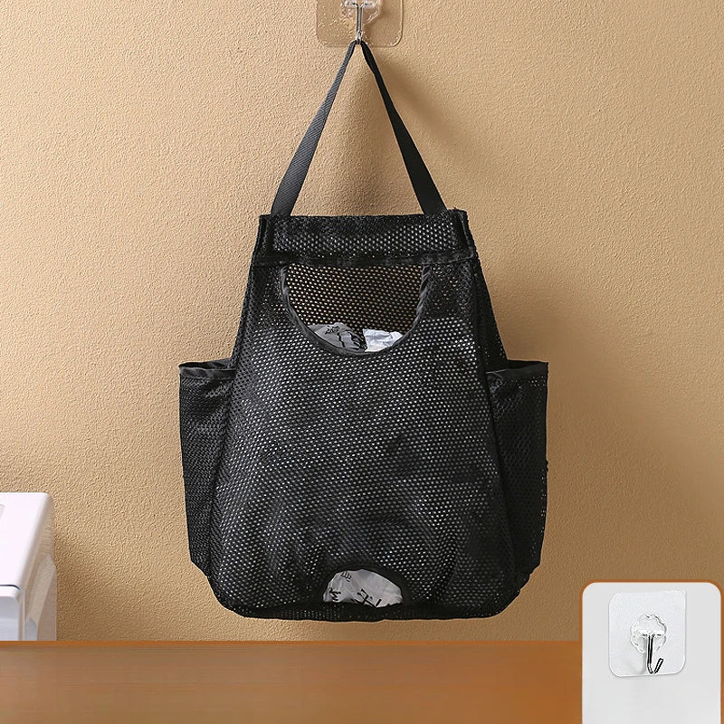 Black mesh bag with handles hanging on a wall, used for garbage bag storage.