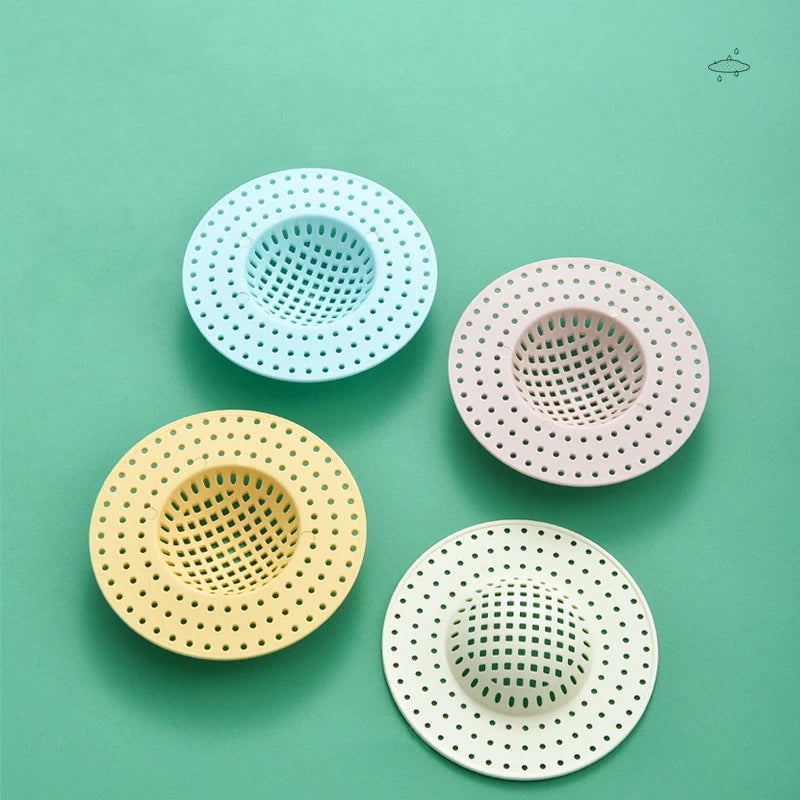 Four circular kitchen sink drain strainers or hair catchers in pastel colors: light blue, pink, yellow, and white.