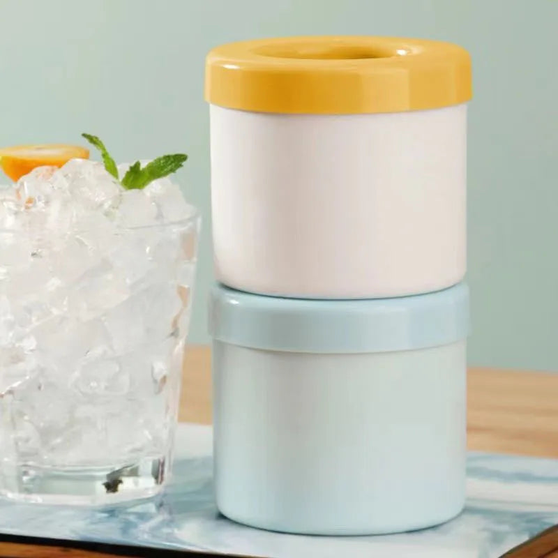 A set of silicone ice cube molds in white and light blue with a yellow lid next to a glass of ice.