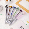 A collection of natural crystal pens featuring various colors including amethyst, quartz, and jade, resting on a white surfac