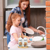 A young girl is helping an adult wash dishes using a Farmhouse Cow Soap Dispenser.