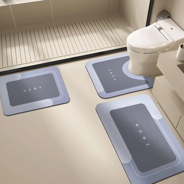 Three gray diatomium mud floor mats placed on a light beige bathroom floor near a toilet.
