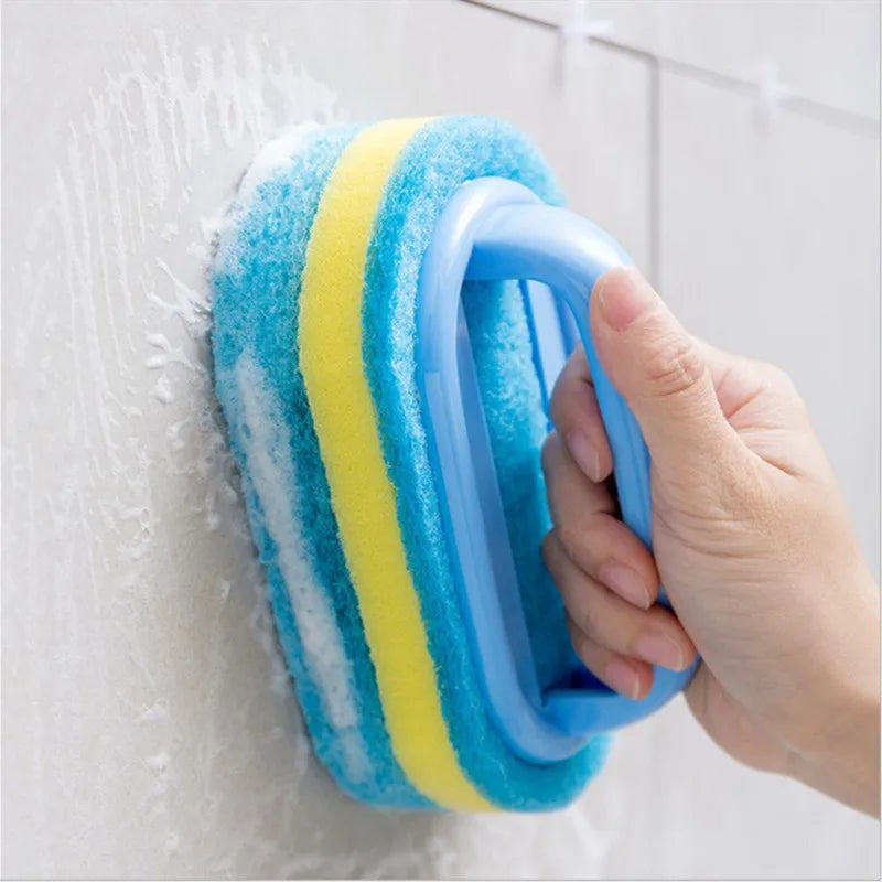 A hand is holding a blue and yellow multi-surface cleaning sponge against a white wall.