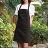 A person wearing a black oil-proof cooking apron over a white shirt standing outdoors.