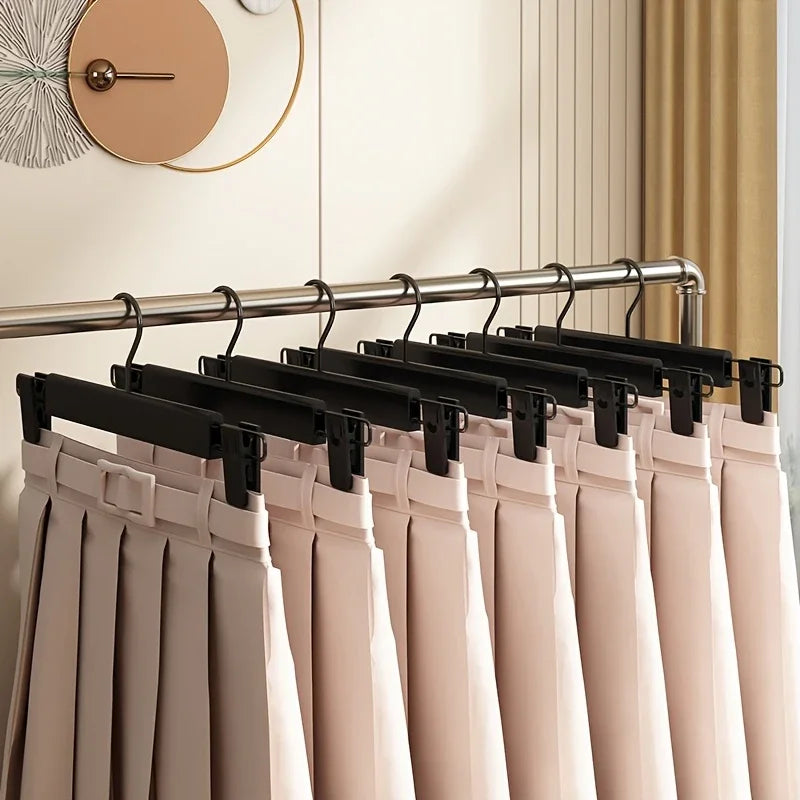 A row of adjustable black clothes hangers with light pink garments hanging on a metal rack.
