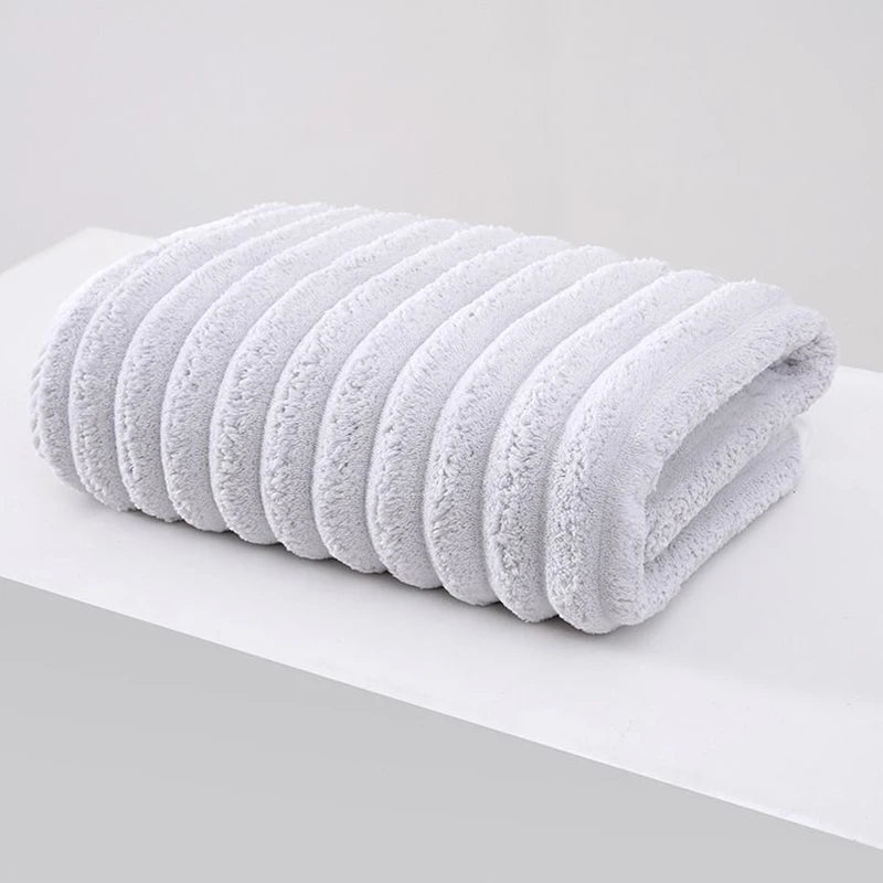 A stack of white thickened microfiber bath towels rolled neatly on a white surface.