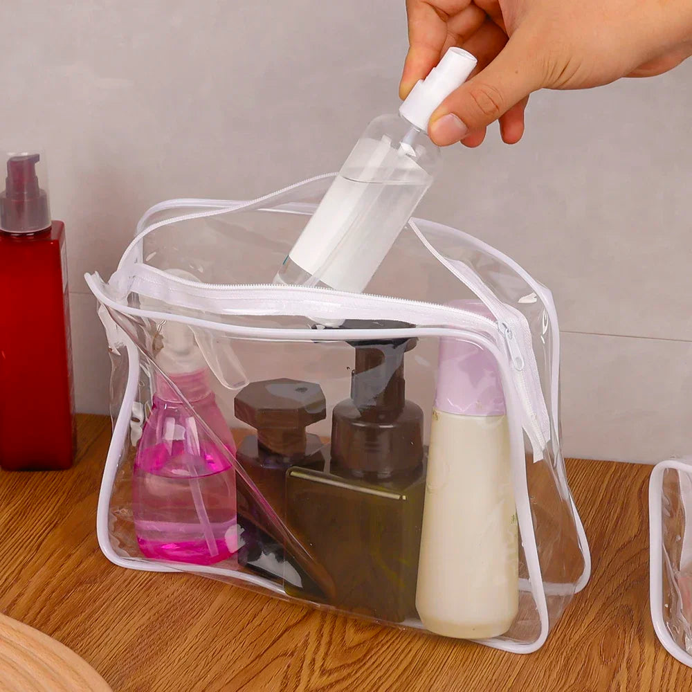 A hand is pouring liquid into a clear plastic travel makeup organizer bag containing three cosmetic bottles.