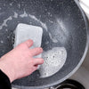 A hand is dipping a gray double-sided cleaning sponge into soapy water in a large metal bowl.