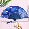 A blue and purple lace fabric folding hand fan displayed on a white background with a green fern leaf nearby.