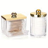 A clear glass apothecary jar dispenser with a golden lid filled with cotton balls and swabs.