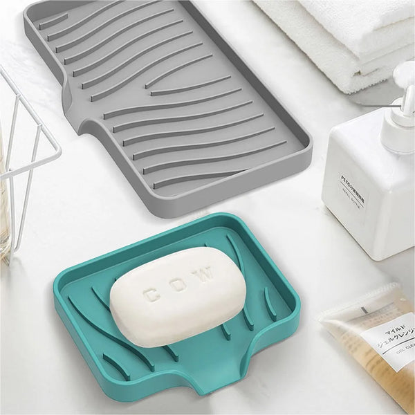 A silicone sink drain tray set featuring a gray ribbed tray and a teal tray holding a white soap bar.
