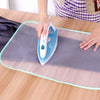 A hand is using a blue heat resistant ironing cloth and press guard on a wooden table.