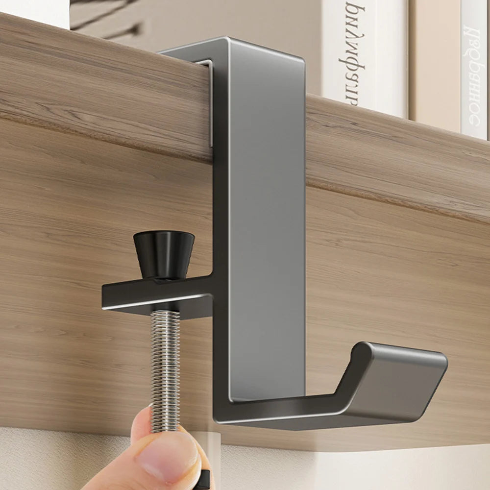 A close-up of a modern gray aluminum desk hanging hook being installed on a wooden cabinet surface.