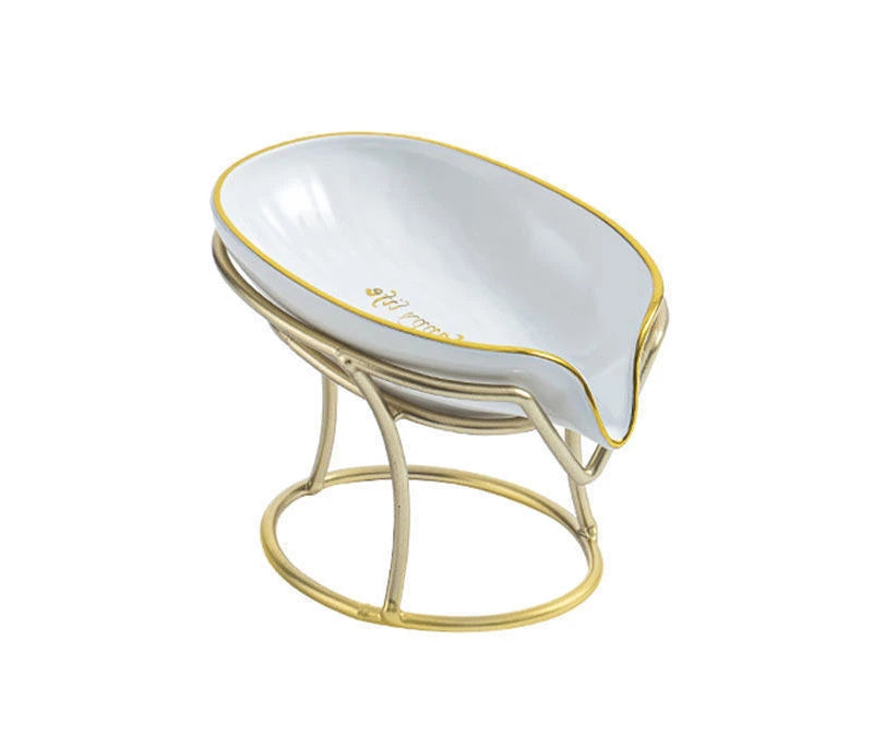 A decorative leaf-shaped soap dish with a white ceramic bowl and gold trim on a metal stand.