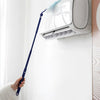 A hand is using a blue electrostatic duster to clean a white air conditioner unit mounted on a wall.