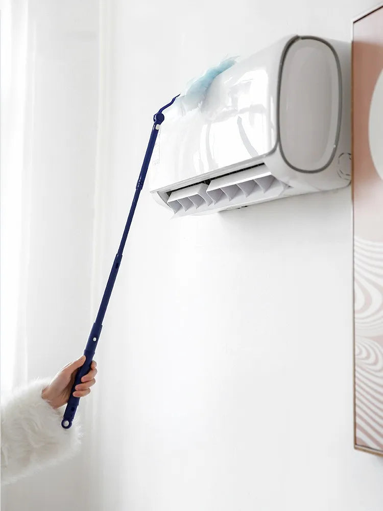 A hand is using a blue electrostatic duster to clean a white air conditioner unit mounted on a wall.