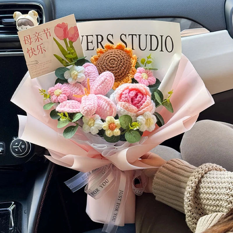A bouquet of handmade pink and yellow crochet flowers wrapped in sheer pink paper sits on a car interior.