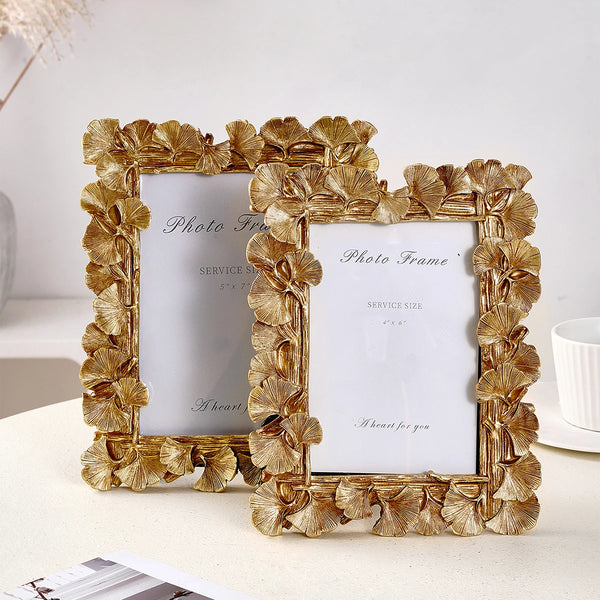 A golden ginkgo leaf photo frame with a white insert, displayed on a light surface.