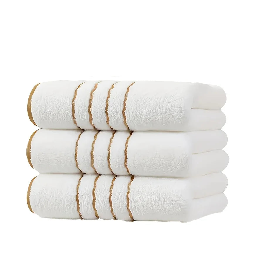 A stack of white Coral Fleece towels with gold stripe detailing.