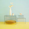 Clear acrylic stackable buffet riser displaying a white vase with yellow flowers and a small ceramic animal figurine.