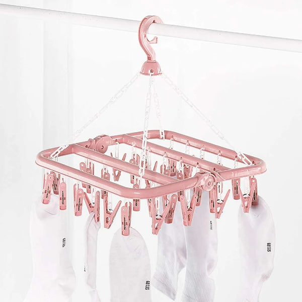 A pink multi-clip clothes drying rack hanging from a rod, with white clothing items visible below.