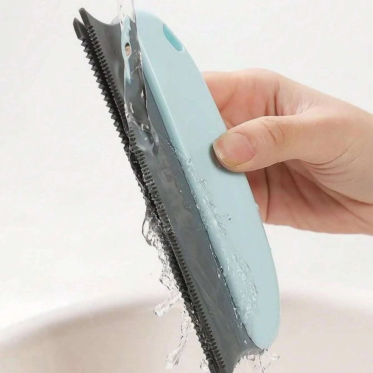 A hand is holding a light blue pet hair remover brush, showing water dripping from the bristles.