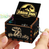 An antique wooden hand crank music box with a Jurassic Park themed lid and dinosaur silhouette inside.