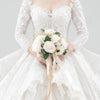 A bride wearing a white lace wedding dress holds an elegant bouquet of white and cream roses.