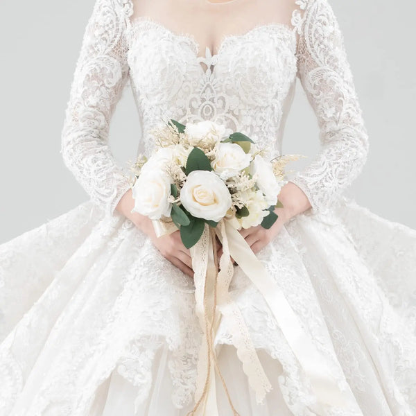 A bride wearing a white lace wedding dress holds an elegant bouquet of white and cream roses.