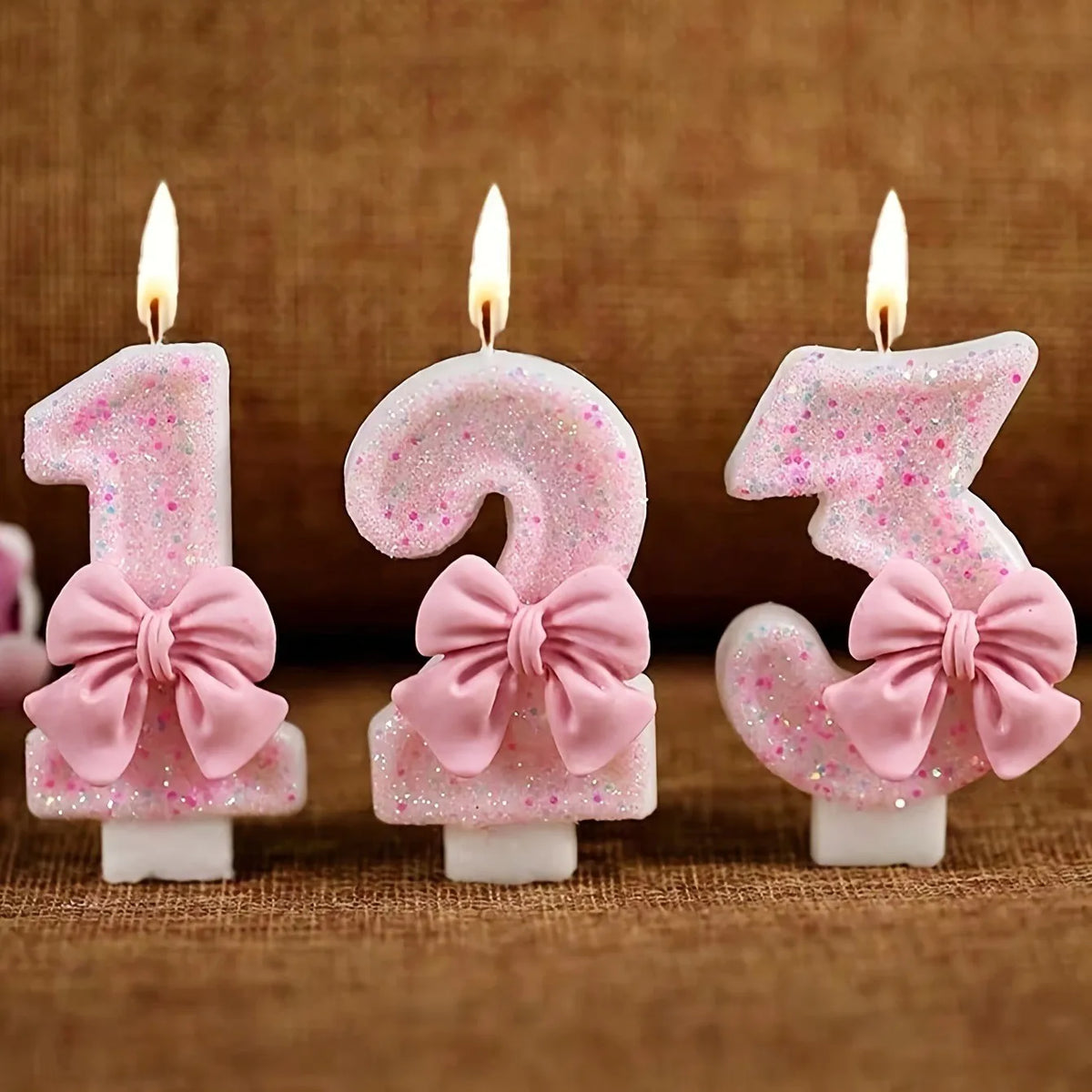 Three pink glitter number candles shaped like 1, 2, and 3 with lit flames