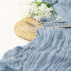 A light blue sheer fabric runner draped next to a woven mat and silver cutlery with white flowers.