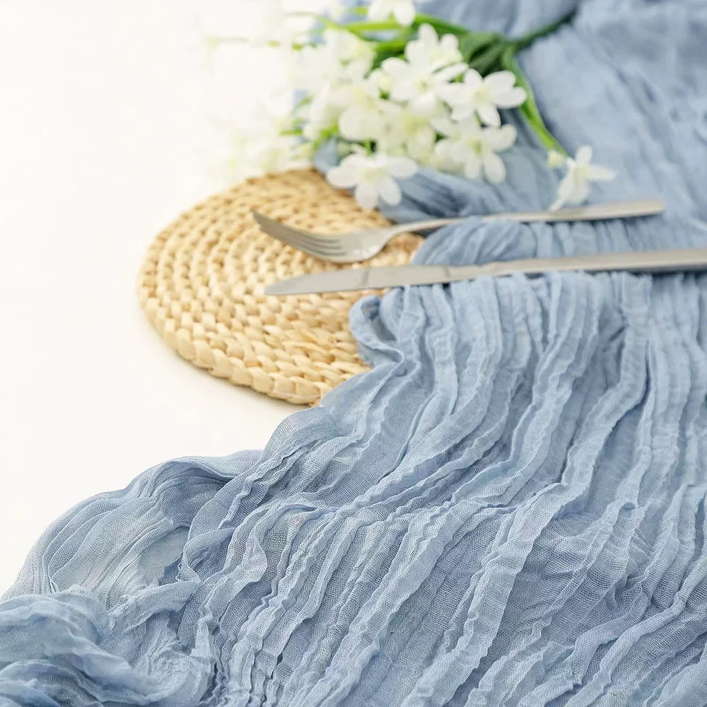 A light blue sheer fabric runner draped next to a woven mat and silver cutlery with white flowers.