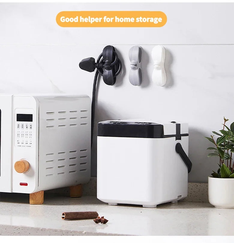 A white reusable cable management organizer is displayed on a countertop next to a white appliance and wall-mounted holders.