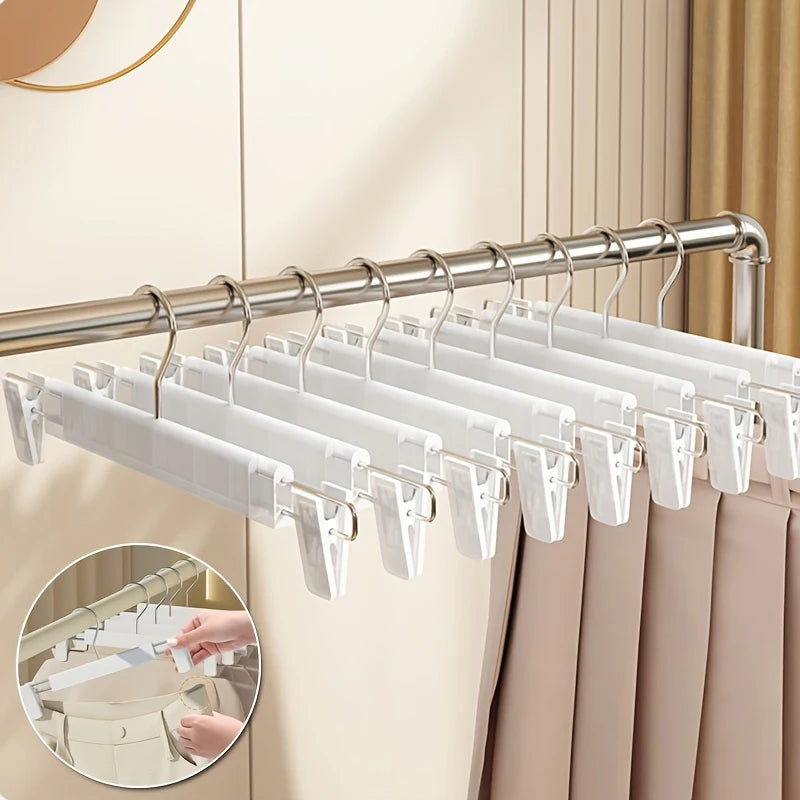 A close-up view of white adjustable clothes hangers hanging on a metal rod against a light beige background.