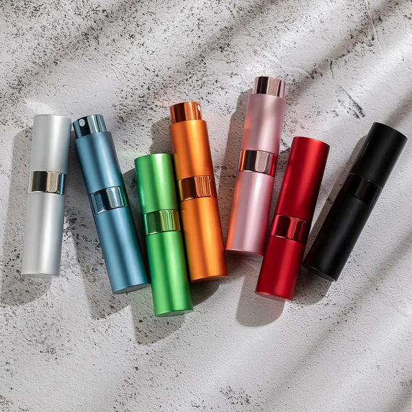 A set of three colorful perfume atomizers in silver, blue, orange, pink, red, and black displayed on a light gray surface.