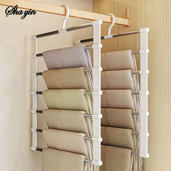 A white multi-layer hanger organizer rack displaying several folded beige pants on a wall.