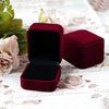 A deep burgundy velvet jewelry box is shown open on a white floral patterned surface.