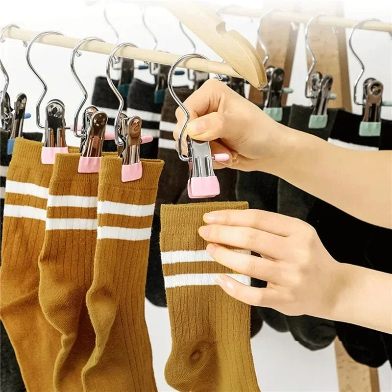 A hand is using a stainless steel clothespin to hang a mustard yellow knitted sock on a clothes rack.
