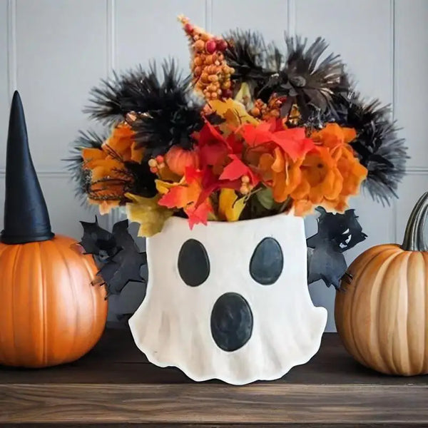 A handmade ceramic ghost vase decorated with black eyes and orange foliage for Halloween decor.