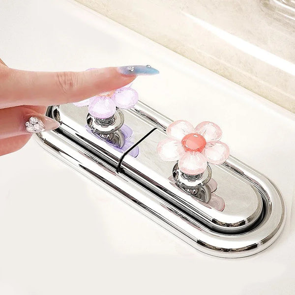 A hand is pressing a decorative flower toilet flush button set on a chrome flush plate.