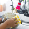 A hand is wiping a stainless steel plate with a yellow plaid microfiber dish towel in a kitchen setting.