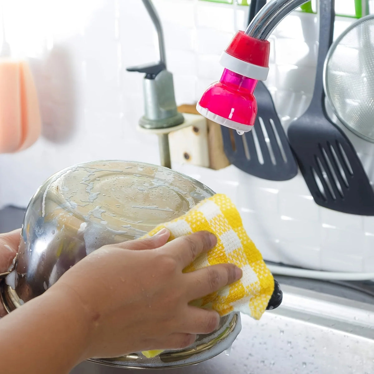 A hand is wiping a stainless steel plate with a yellow plaid microfiber dish towel in a kitchen setting.