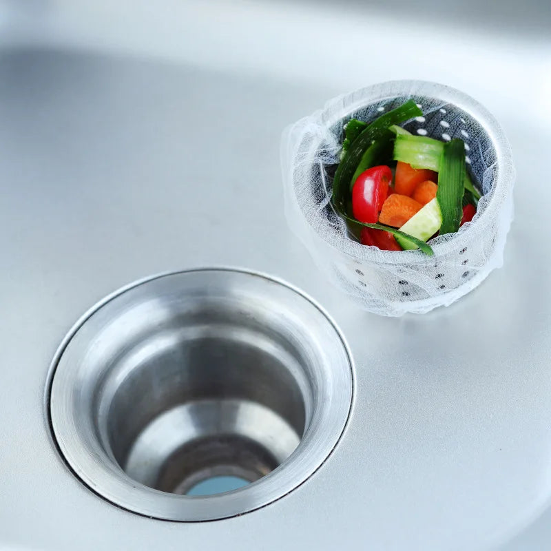 A clear mesh filter bag containing fresh vegetables is placed inside a metal sink drain.