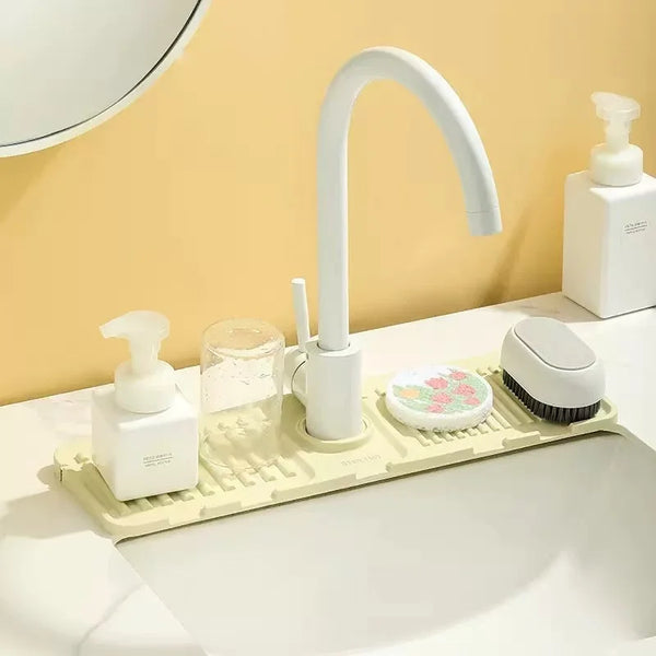 A white splash guard mat for faucets is shown on a countertop next to a white faucet and brush.