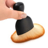A hand holds a black multi-surface cleaning brush with a golden-tipped bristles.